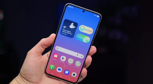 Dłoń trzyma telefon Samsung z widocznymi ikonami aplikacji i widżetem pogody. Ustawienia telefonu Samsung są łatwo dostępne.