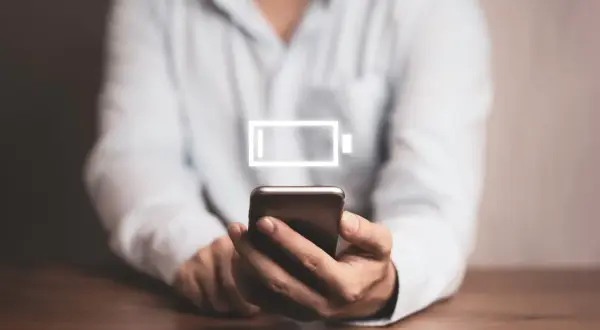 Osoba trzyma smartfon z ikoną niskiego poziomu baterii. Dowiedz się, jak wyłączyć optymalizację baterii Samsung, by dłużej cieszyć się energią.