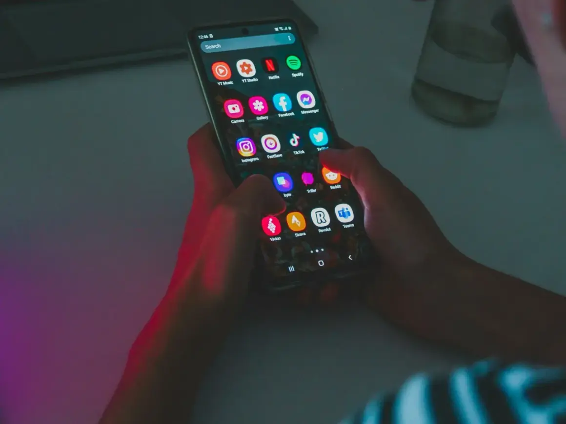 Dłonie trzymają smartfon z ikonami aplikacji, w tym Instagram i TikTok. Wskazówka do oszczędzania baterii: wyłącz niepotrzebne aplikacje.