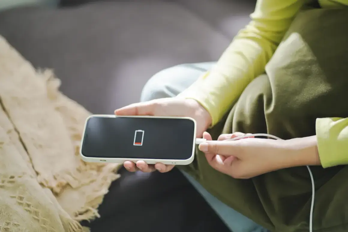 Dramatyczny spadek baterii przez noc na iPhonie. Czerwony wskaźnik pokazuje prawie zerowy poziom naładowania, a użytkownik podłącza ładowarkę.