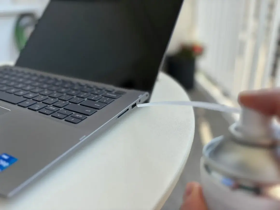 Czyszczenie laptopa z kurzu sprężonym powietrzem. Dmuchawa wylatuje z puszki w kierunku szczeliny obok klawiatury.