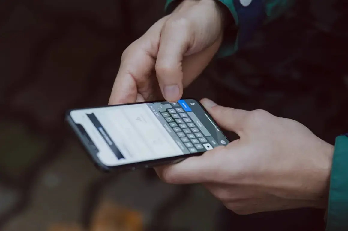Dłonie trzymające smartfon, na ekranie klawiatura. Dowiedz się, jak zmienić czcionkę w telefonie, aby spersonalizować wygląd.