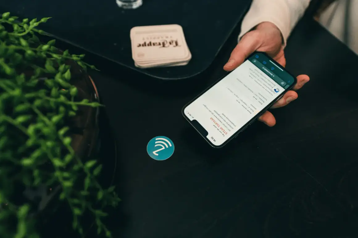 Dłoń trzyma smartfon z menu restauracji, obok symbol NFC. To pokazuje, jak działa NFC, co to jest i jak ułatwia płatności.
