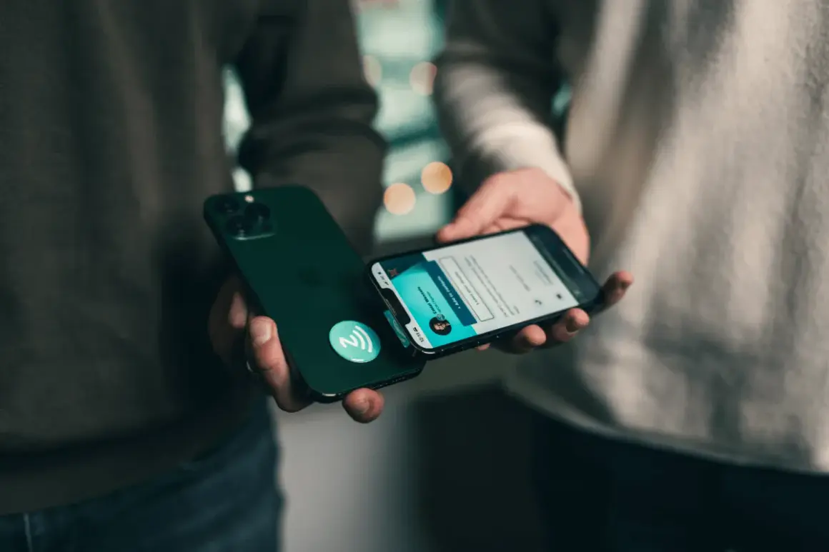 Dwie osoby zbliżają do siebie iPhone'y, jeden z nich ma naklejkę z symbolem NFC.
