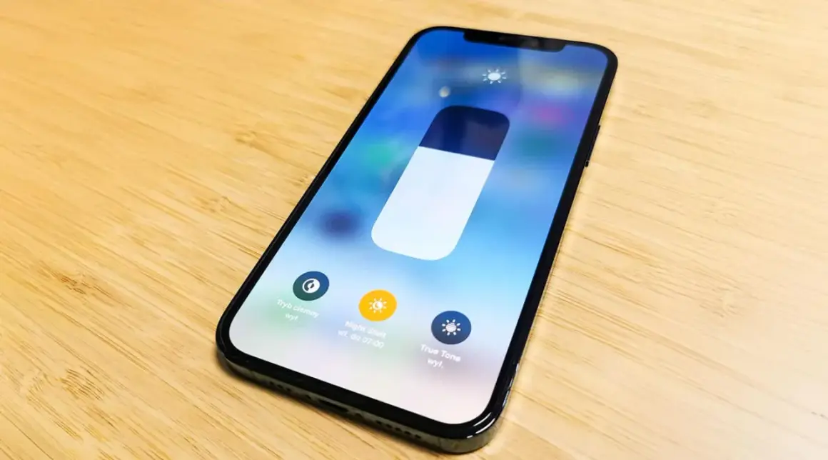 Na ekranie iPhone'a widać suwak jasności i opcje: Tryb ciemny, Night Shift i True Tone. Dowiedz się, jak zmienic kolor godziny w iPhone.