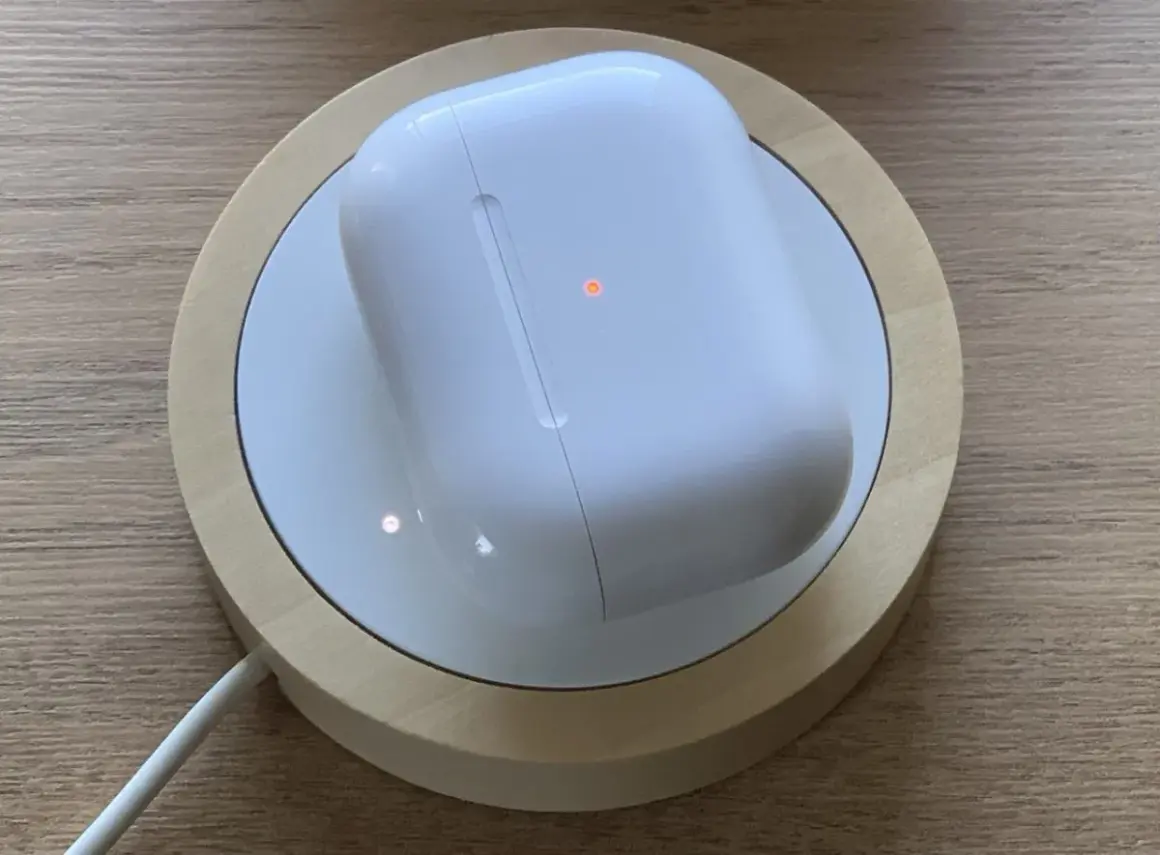 Białe etui AirPods na ładowarce bezprzewodowej, z pomarańczową diodą. Dowiedz się, jak czyscic airpods, by wyglądały jak nowe.