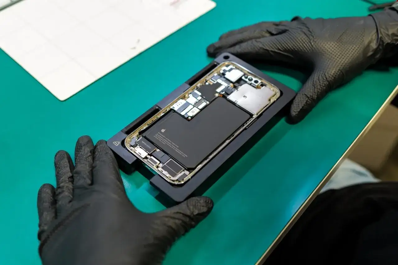 Ręce w czarnych rękawiczkach trzymają rozłożony telefon, gotowy do naprawy. To proces, który może przywrócić mu życie, jak w przypadku urządzeń refurbished po polsku.