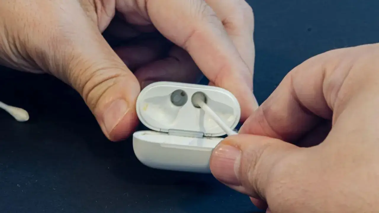 Dłonie czyszczą etui AirPods patyczkiem higienicznym. Dowiedz się, jak czyścić AirPods, aby służyły dłużej.