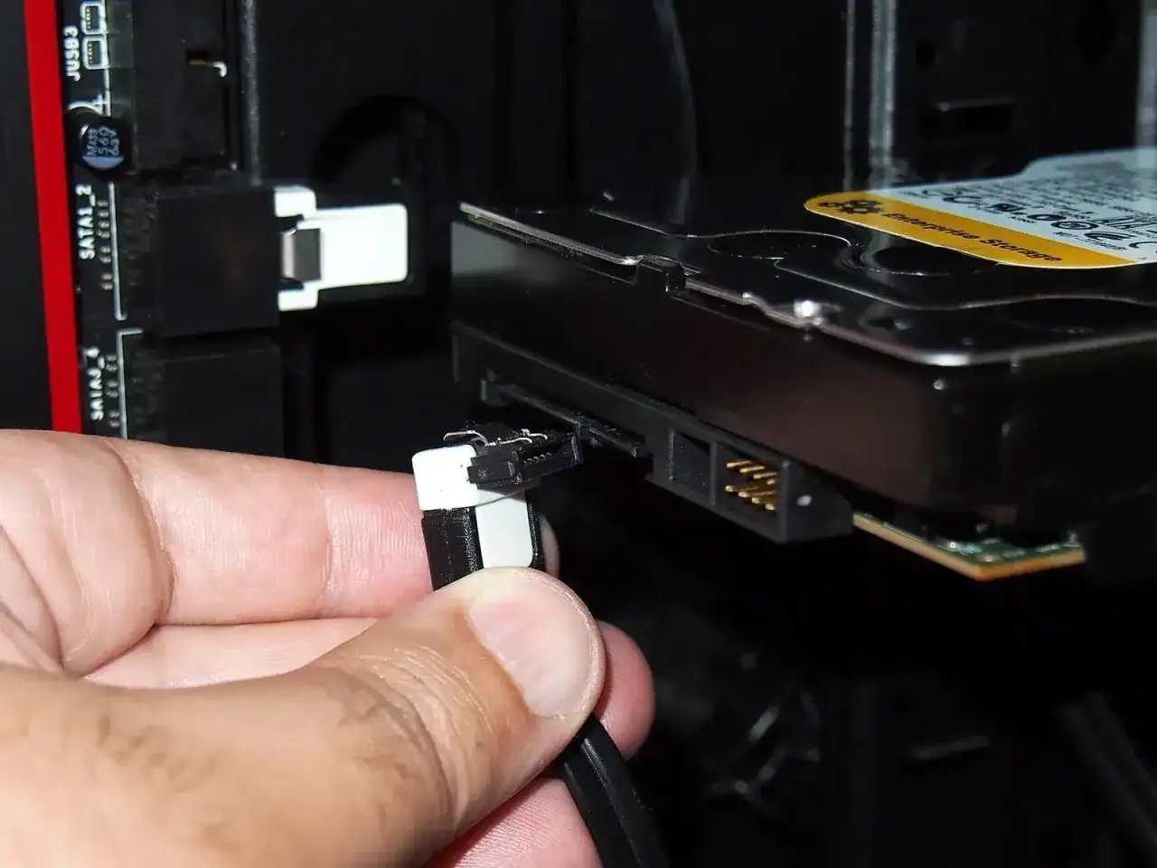 Dłoń podłącza kabel SATA do dysku HDD, pokazując jak podłączyć dysk HDD do komputera.