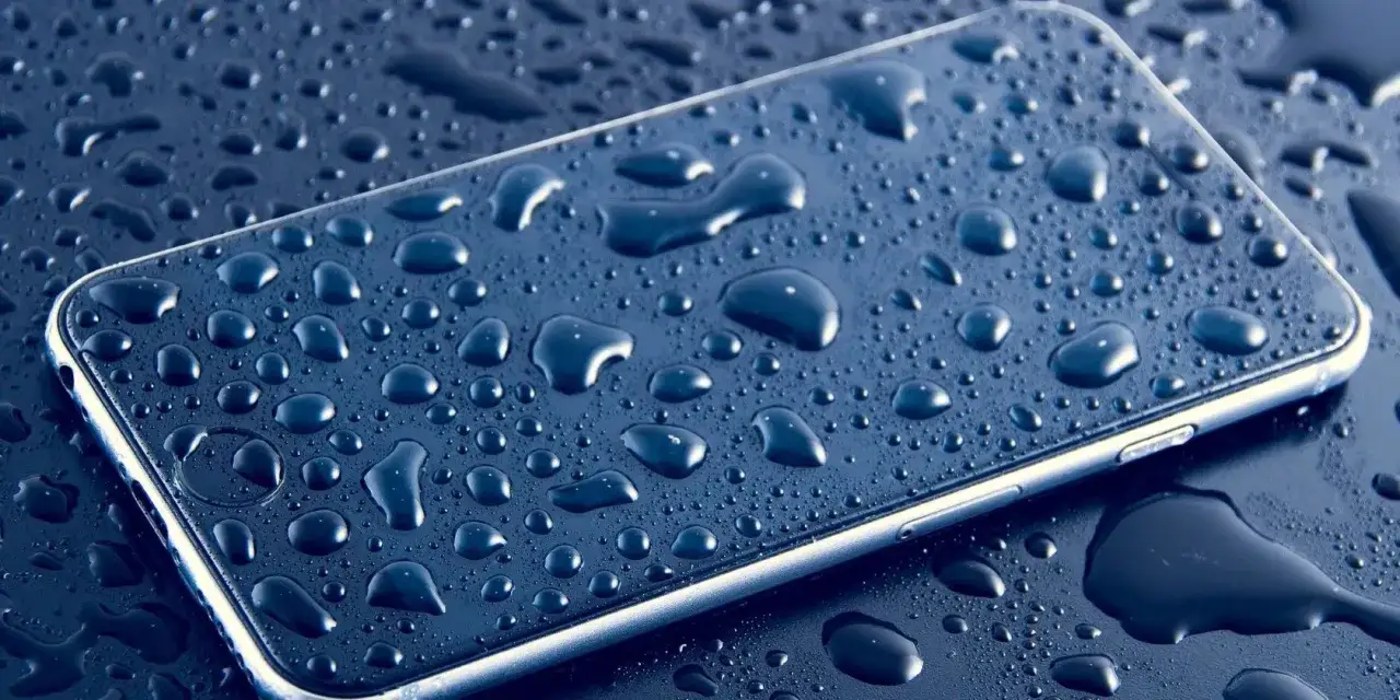 Telefon pokryty kroplami wody. Dowiedz się, jak wysuszyć telefon po zalaniu, aby uratować go przed uszkodzeniem.