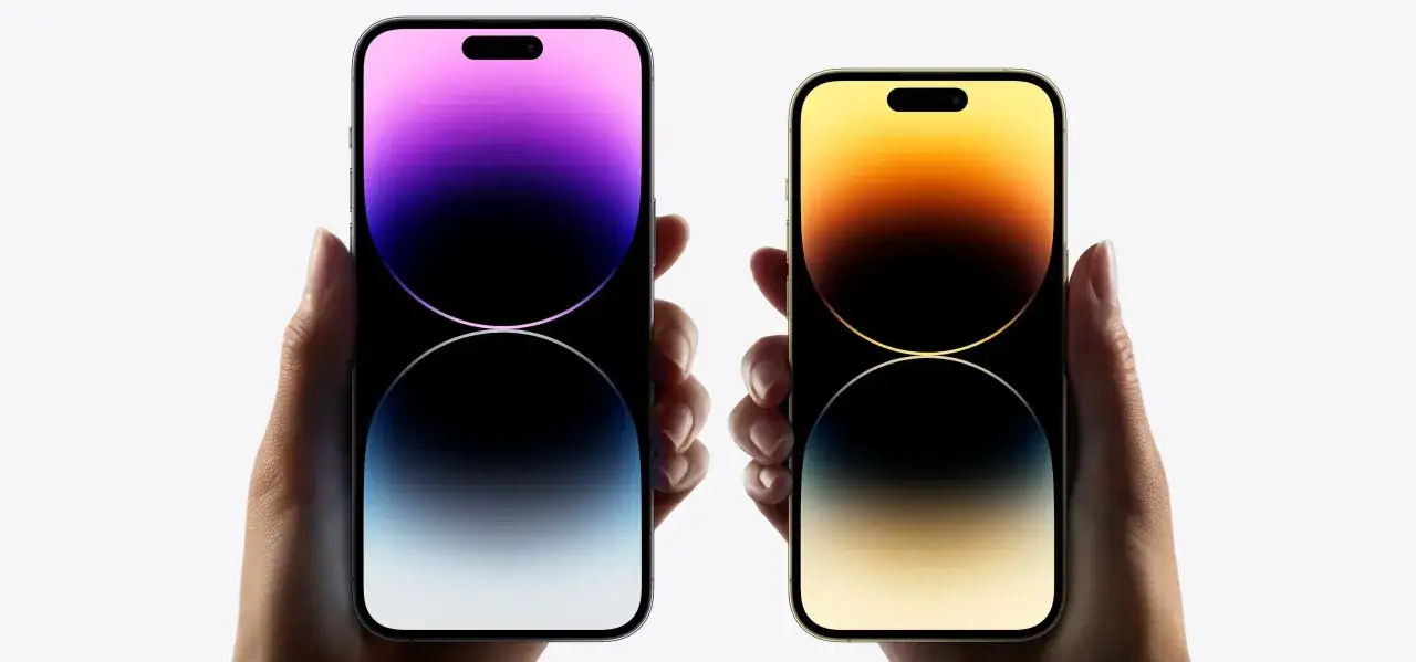 Dwie dłonie trzymają iPhone'y 14 z gradientowymi tapetami. Widoczny efekt odświeżania ekranu.