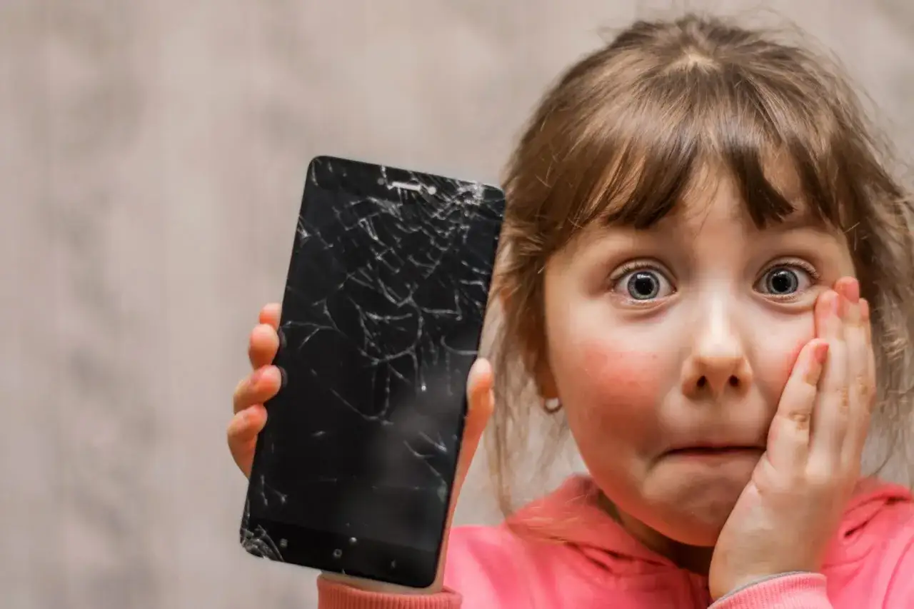 Przerażona dziewczynka pokazuje pęknięty ekran telefonu. Jak usunąć rysy ze szkła hartowanego?