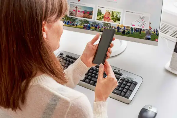Kobieta trzyma smartfon, przygotowując podłączenie telefonu do monitora. Na ekranie widać zdjęcia z wydarzenia.