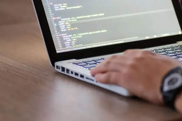 Dłoń programisty pisze kod na laptopie, co może być częścią procesu, jak sprawdzić wydajność laptopa.
