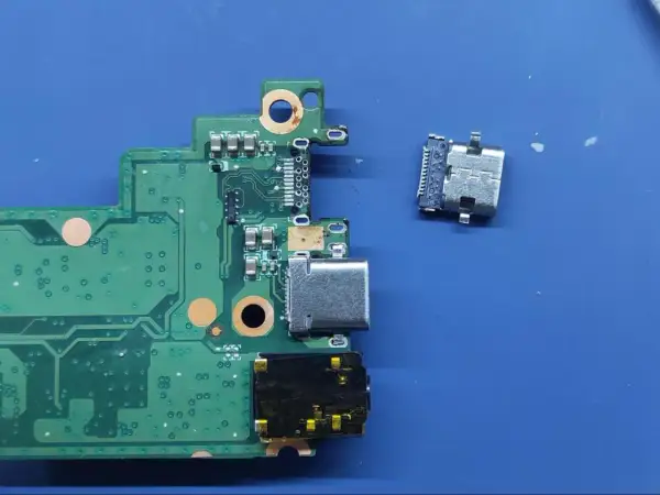Luźne gniazdo USB C obok płyty głównej. Naprawa laptopa wymaga precyzji.