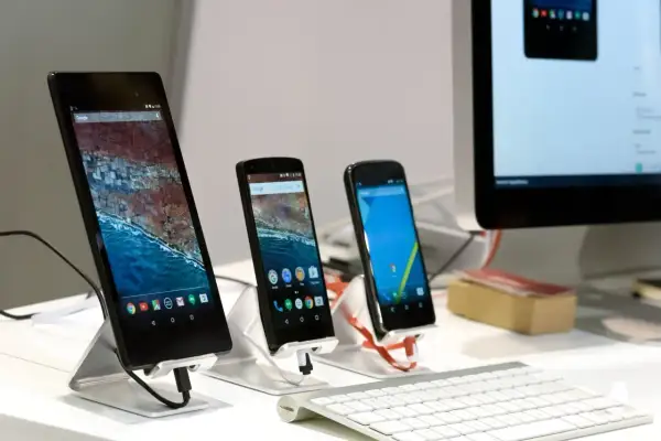 Na biurku stoją trzy smartfony i tablet, a obok klawiatura i monitor komputera. Można wysłać sms na komputerze.