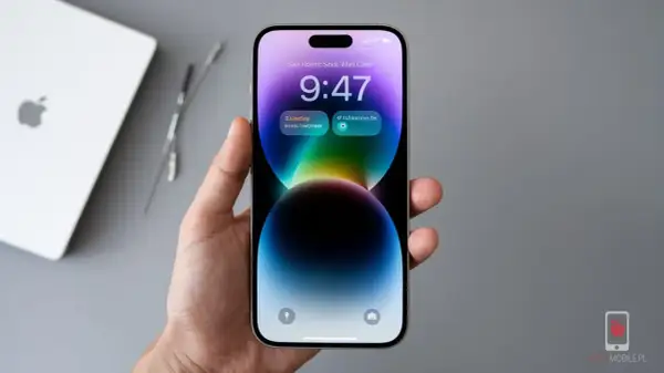 Dłoń trzyma iPhone 14 z kolorową tapetą i widoczną godziną 9:47. Ekran odświeżanie jest płynne.