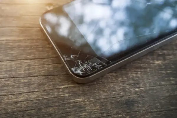 Zbity ekran telefonu leży na drewnianym blacie. Pęknięcia tworzą pajęczynę na szkle, świadcząc o niefortunnym upadku.