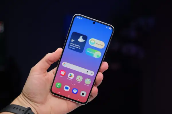 Dłoń trzyma smartfon Samsung z kolorowym ekranem. Widoczne widżety pogody i wiadomości, ikony aplikacji. Dbałość o ochronę baterii Samsung jest kluczowa.