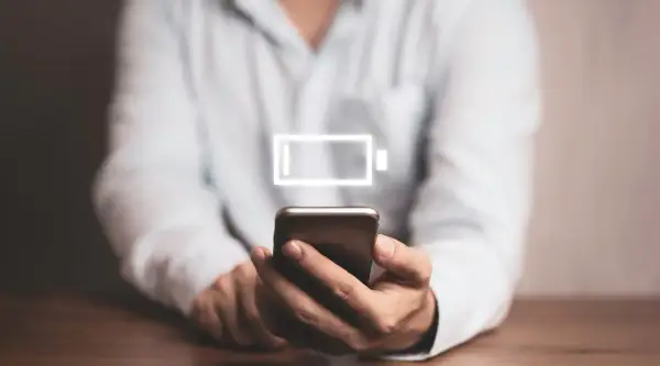 Osoba trzyma smartfon z ikoną niskiego poziomu baterii. Dowiedz się, jak wyłączyć optymalizację baterii Samsung, by dłużej cieszyć się energią.
